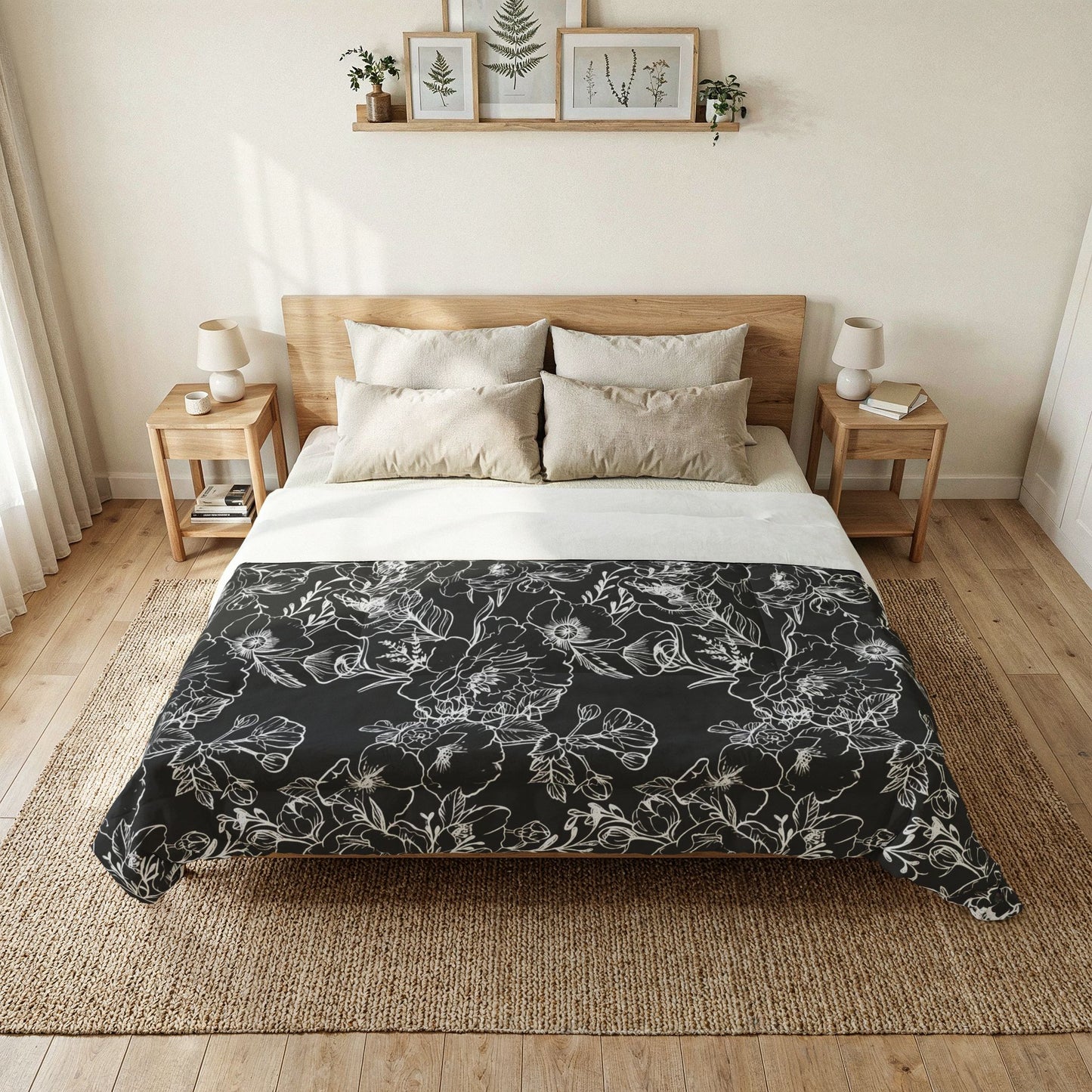 A neatly made bed in a bright, minimalist bedroom, featuring a black comforter with a white floral line-art pattern over white sheets and beige pillows.